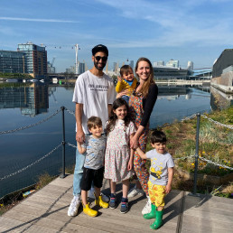 The Solanki family, made up of four children and two adults stand in front of the Royal Docks on a sunny day.