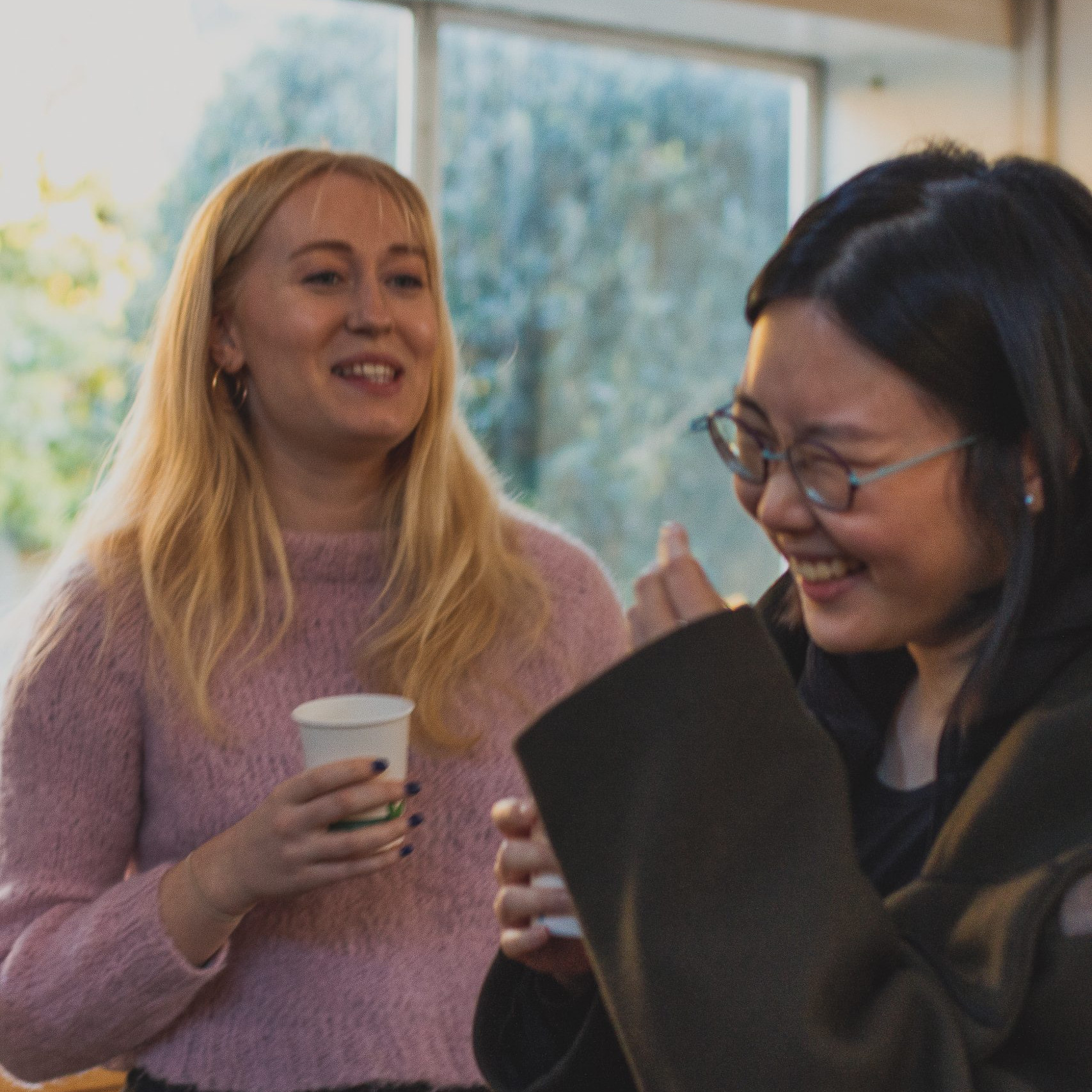 Two girls laughing at a joke with a coffee cup in hand