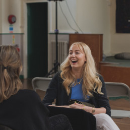 Young blonde woman relaxes on a chair and laughs with a friend in church.