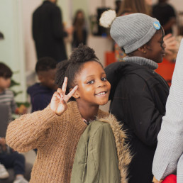 Young girl holds up peace sign and smiles for the camera with a backdrop of many people at church