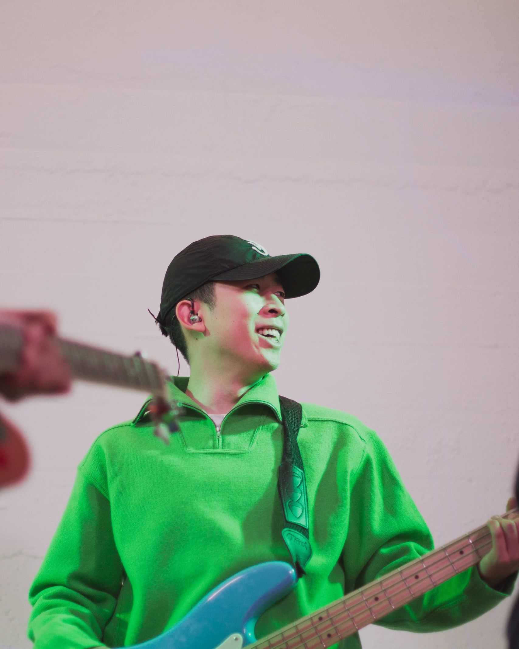 Young man in a green top with a blue bass guitar is looking to the left and smiling.